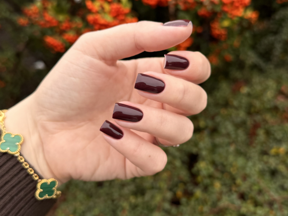 Donker bordeauxrode amandelnagels tegen een herfstachtige achtergrond