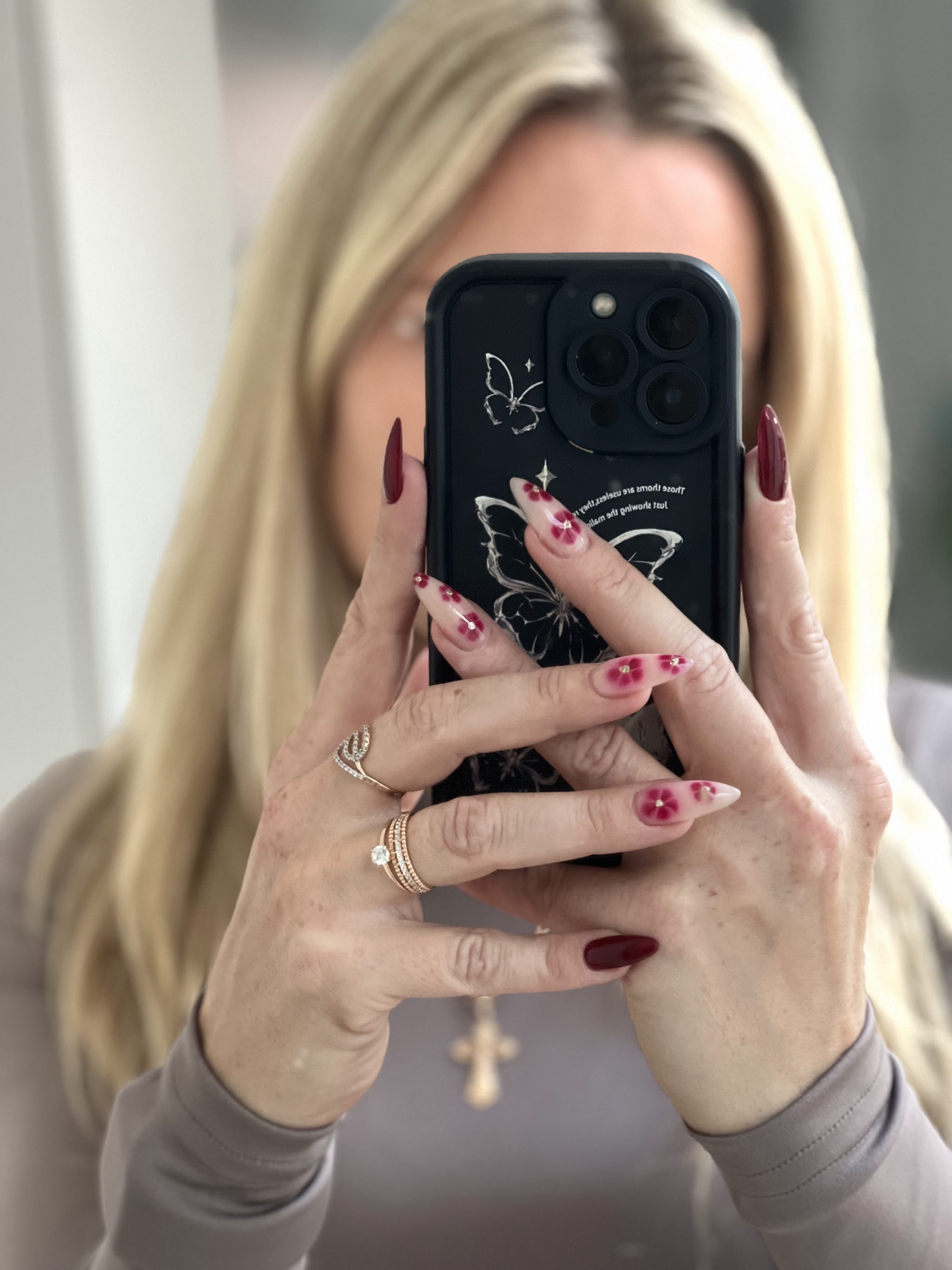 Bordeauxrode amandelnagels met hartjes, de klant houdt haar telefoon voor haar gezicht