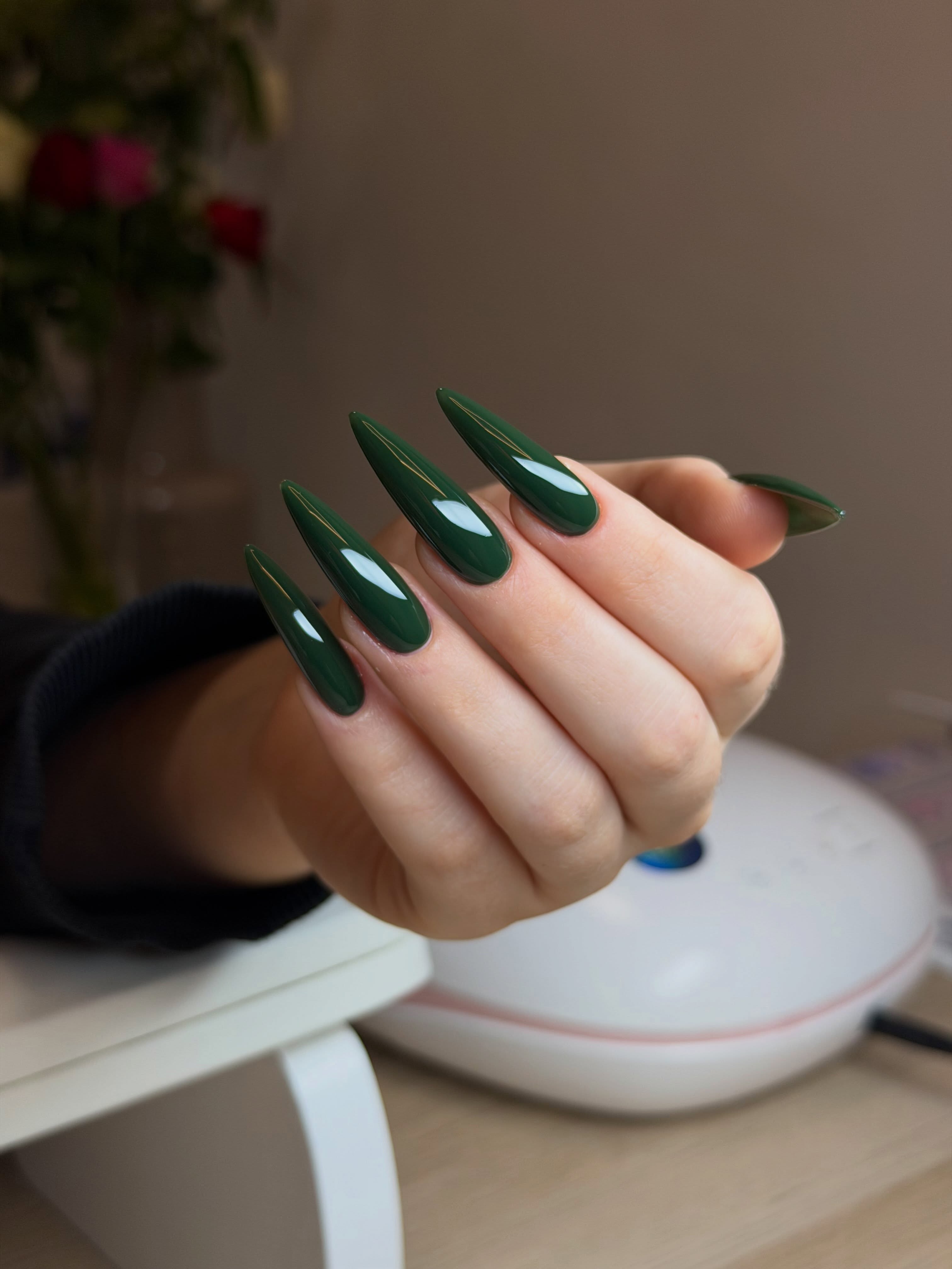 Lange donkergroene glanzende stiletto-nagels onder de lamp aan Daria's tafel